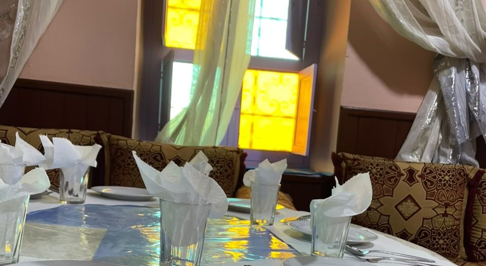 The guesthouse restaurant in Tagmoute: a laid table, Moroccan benches and a window with coloured stained glass