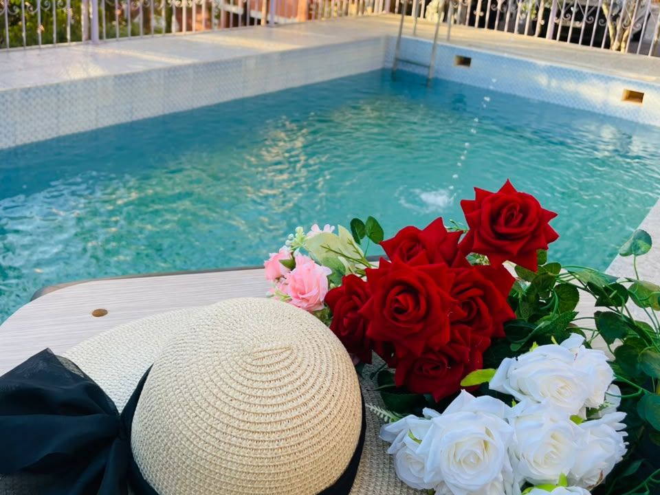 La piscine de l'Auberge Pied du Siroua à Tagmoute, avec un bouquet de roses et un chapeau de paille au bord de l'eau
