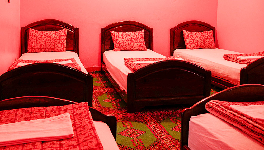 Chambre familiale de l'auberge : lits simples en bois, couvertures rouges et tapis berbère
