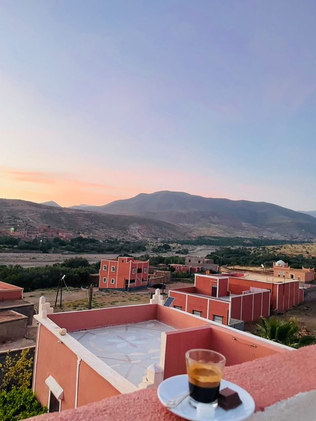 Café et carré de chocolat sur la terrasse rose de l'auberge, face au village de Tagmoute et aux montagnes au coucher du soleil