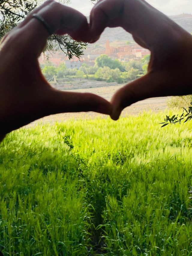 Deux mains formant un cœur autour du village de Tagmoute, au-dessus d'un champ vert