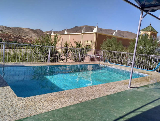 Piscine de l'auberge entourée d'une balustrade blanche, face aux montagnes et au village de Tagmoute