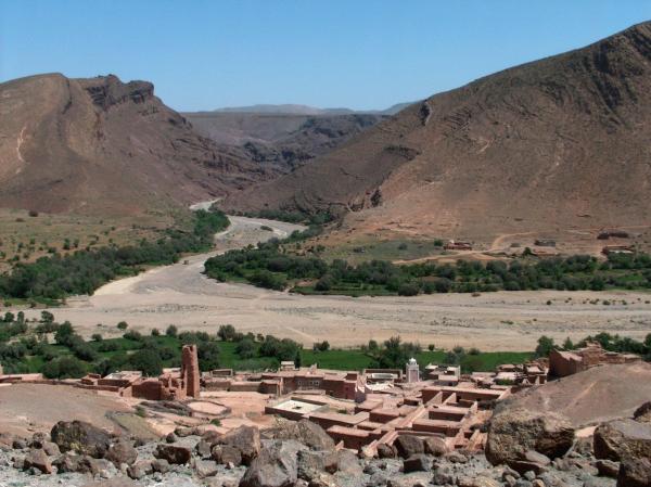 Vallée et lit d'oued à sec bordés de cultures, au pied de montagnes arides, avec un village en terre au premier plan, région de Tagmoute